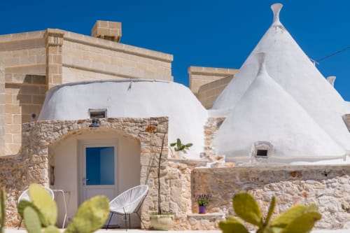 Villa trulli imbiancata a calce a Ostuni con arco in pietra, porta azzurra e zona lounge sotto cielo sereno