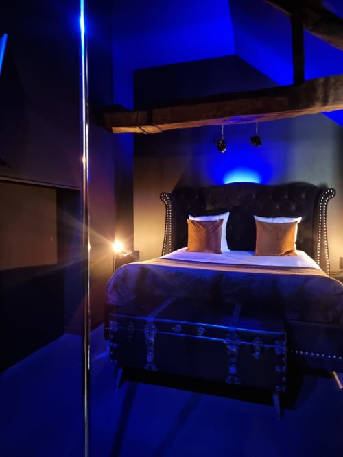 Chambre moderne à La Maison Defendue avec éclairage ambiant bleu, tête de lit capitonnée noire et poutre en bois rustique