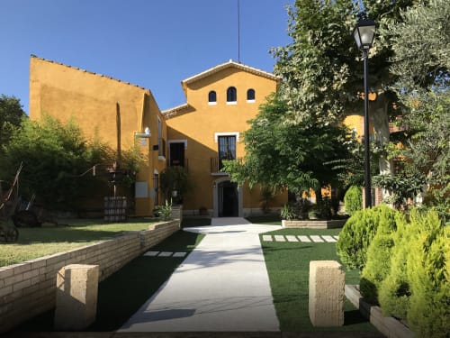 Entrada de la villa Masias Can Trabal en Olèrdola con fachada amarilla, jardines cuidados y camino de piedra hacia la puerta principal