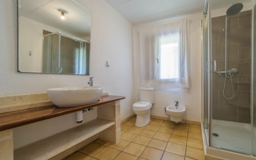 Baño espacioso en villa Masia Can Trabal con lavamanos redondo, inodoro, bidé y ducha con azulejos de terracota