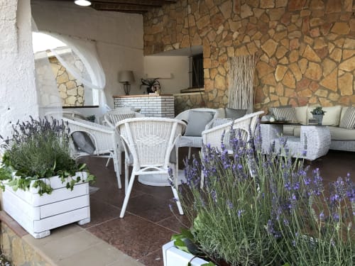 Patio rústico de piedra en villa Masias Can Trabal con mobiliario de mimbre blanco, lavanda morada y cómoda zona de descanso