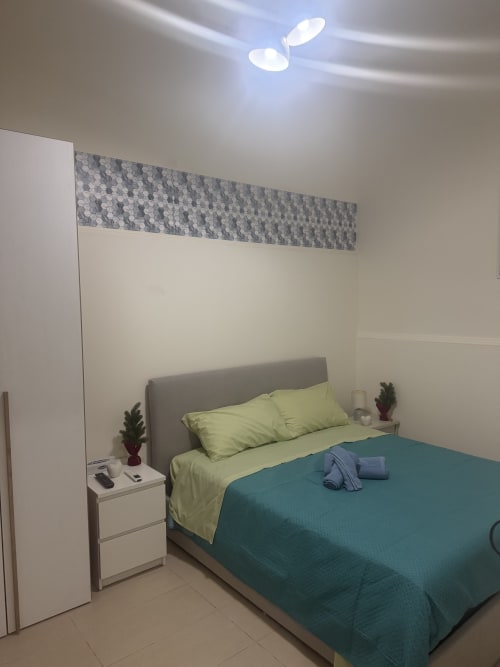 Camera moderna alle Sidra Apartments Bari con letto matrimoniale, biancheria lime, plaid teal, testata grigia e comodino bianco