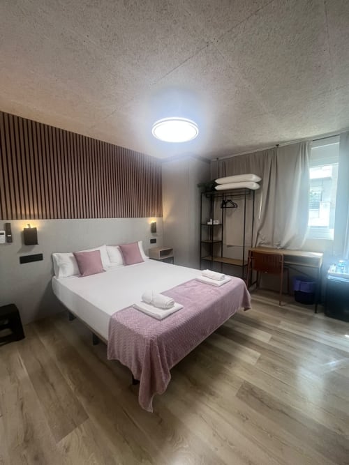 Modern hotel room at Hostal Abacoa in Alicante with queen bed, pink accents, wooden floors, and contemporary lighting