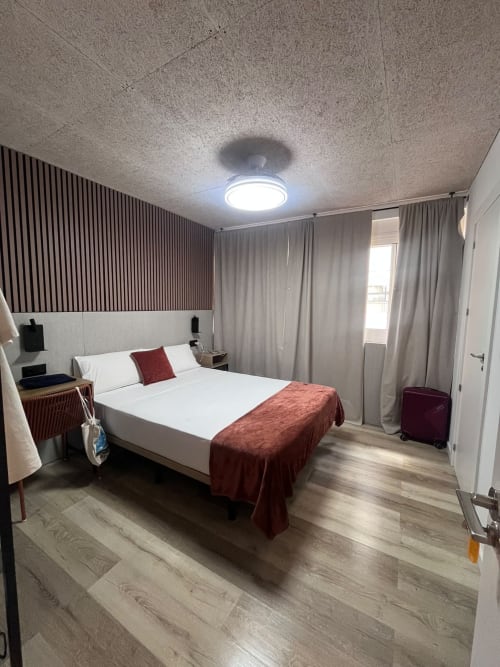 Habitación moderna en Hostal Abacoa, Alicante, con cama queen, manta roja, vista a la ciudad y mobiliario contemporáneo