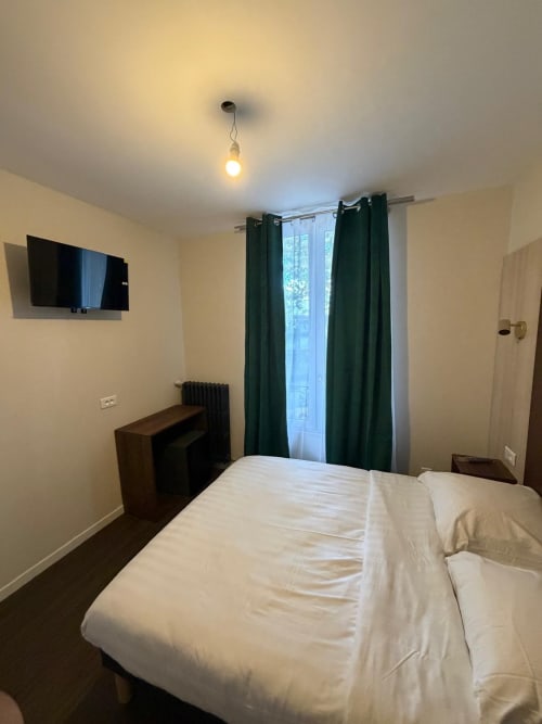Chambre de l'Hôtel le Dellys à Colombes avec lit, télévision, rideaux vert foncé et équipements modernes