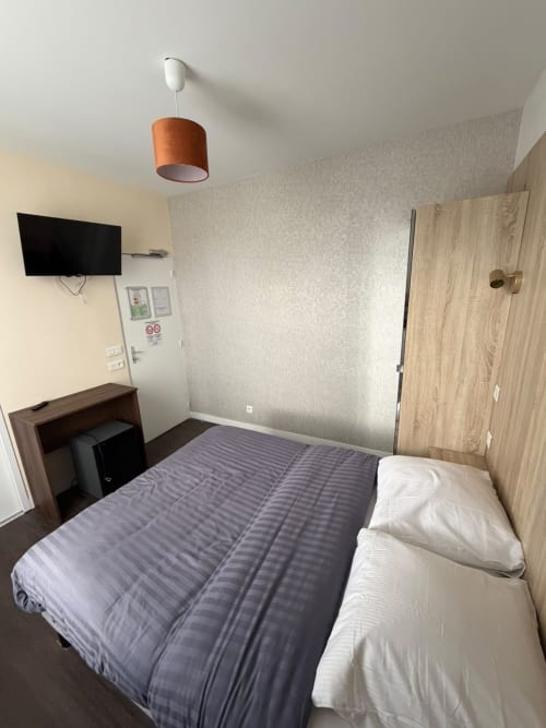 Chambre d'hôtel moderne à l'Hôtel le Dellys à Colombes avec lit, bureau, télévision et luminaire suspendu orange