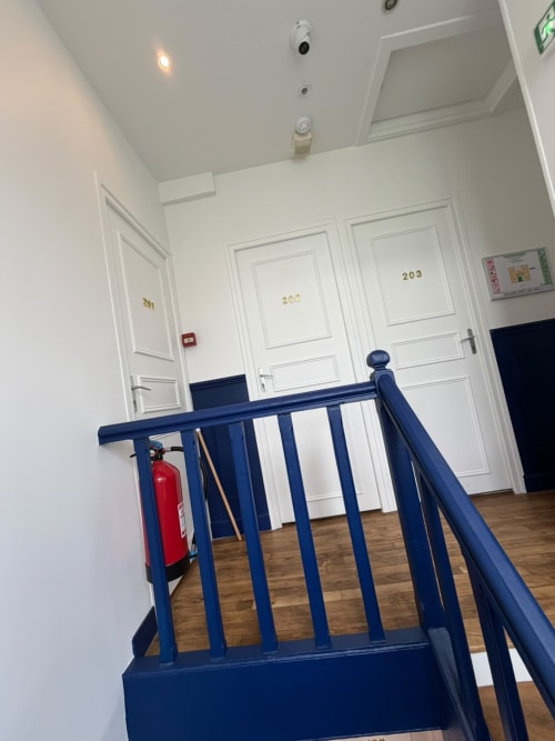Couloir d'hôtel avec rampe bleue, portes blanches numérotées 203, parquet, extincteur à l'Hôtel le Dellys Colombes