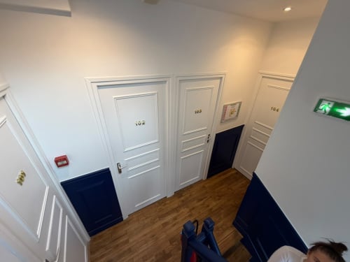 Couloir de l'Hôtel le Dellys à Colombes avec portes numérotées, murs blancs, sol en bois et panneau de sortie de secours