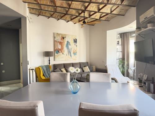 Moderno salón de apartamento en Valencia con mesa de comedor, sofá gris, obras de arte y diseño de techo con efecto paja
