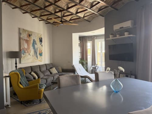 Elegante sala de estar en Valencia con sofá gris, sillón amarillo, TV y vistas a la ciudad
