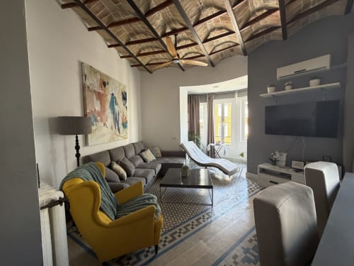 Apartamento de lujo moderno en Ciril Amorós de Valencia con sofá gris, sillón amarillo, TV, techo de madera y vistas a la ciudad