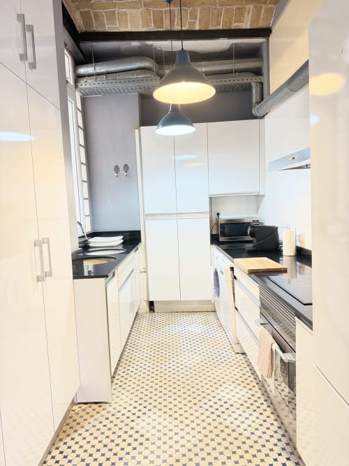 Cocina moderna blanca con encimeras negras en lujoso apartamento de Valencia, luces colgantes