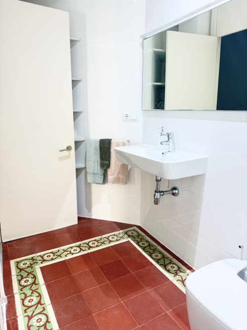 Cuarto de baño moderno en apartamento Stay Gest, Valencia con lavabo blanco, espejo, suelo de azulejos rojos con cenefa decorativa y almacenaje