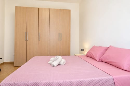 Camera da letto con letto rosa presso gli Apartamenti Sidra a Bari, con armadio in legno e asciugamani piegati