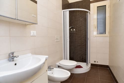 Bagno moderno negli Apartamenti Sidra di Bari con box doccia, wc, bidet, lavabo e pavimento in piastrelle marroni.