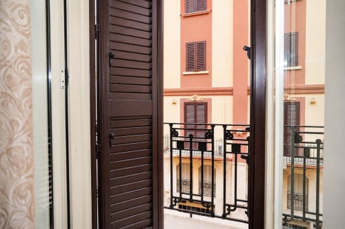 Balcone dell'Aparthotel Sidra a Bari con porte a persiane in legno scuro che si aprono su ringhiera in ferro battuto affacciata su terracotta