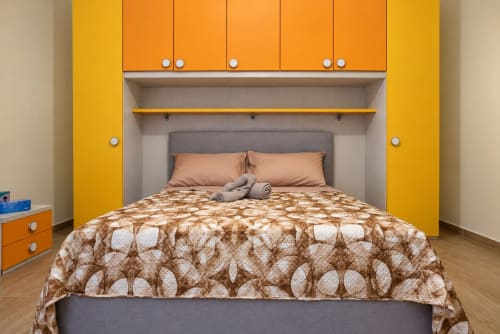Camera da letto colorata al Sidra Apartments Bari con mobili gialli, porte arancioni, biancheria a fantasia e arredi moderni