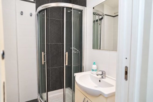 Bagno moderno presso Sidra Apartments Bari con doccia in vetro curvo, lavabo bianco e dettagli in piastrelle scure