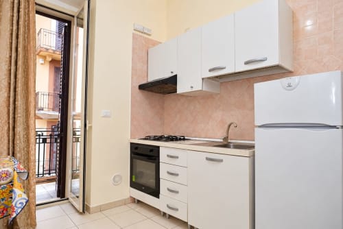 Cucina moderna con mobili bianchi, fornello a gas, frigorifero e rivestimento rosa negli Appartamenti Sidra, Bari