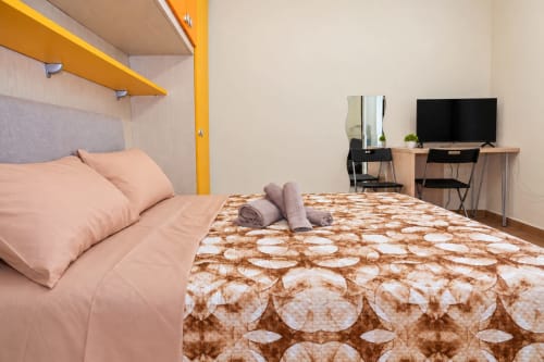 Sidra Apartments Bari - monolocale moderno con biancheria color pesca, copriletto fantasia, ripiani gialli, scrivania con TV e vista città
