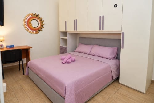 Camera moderna alle Sidra Apartments Bari con biancheria rosa, armadio integrato, scrivania in legno e specchio sole oro