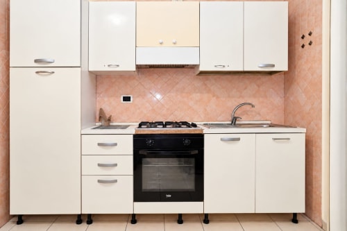 Cucina moderna negli Apartamenti Sidra di Bari con mobili bianchi, rivestimento in piastrelle color pesca, fornello a gas e lavello