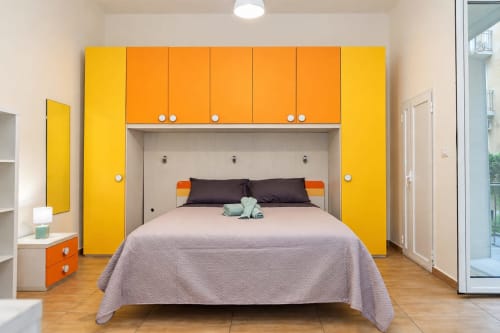 Camera moderna e colorata alle Sidra Apartments Bari con armadio giallo e arancione, letto matrimoniale e balcone con vista città