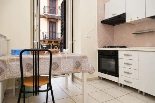 Cucina moderna con zona pranzo negli Appartamenti Sidra, Bari. Mobili bianchi, fornello nero, tovaglia decorata, vista sulla città