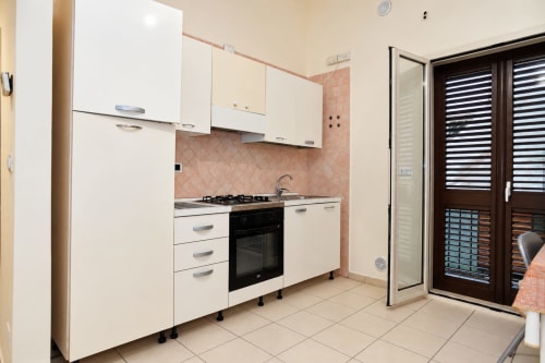 Cucina moderna negli Sidra Apartments a Bari con mobili bianchi, fornello nero, schienale in cotto e porte vetrate verso la terrazza