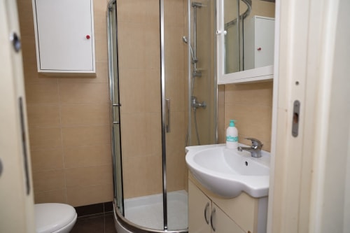 Bagno moderno negli Apartamenti Sidra di Bari con doccia in vetro curvo, lavabo bianco e piastrelle beige