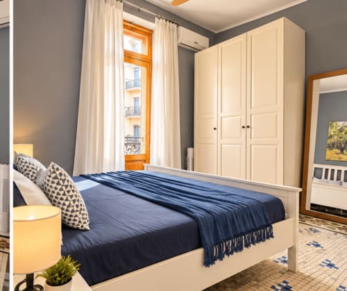 Lujosa habitación en apartamento de Valencia con armario crema, ropa de cama azul marino, marco de ventana de madera y vistas a la ciudad