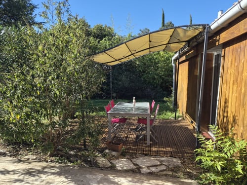 Terrasse de restaurant en plein air du Domaine en Terre Happy avec auvent jaune, terrasse en bois et vue sur le jardin à Labastide-de-Virac