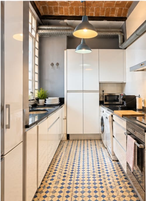 Moderna cocina al galley en apartamento de Valencia con gabinetes blancos, encimeras negras, azulejos geométricos e industrial