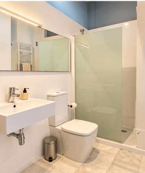 Baño moderno en apartamento de lujo de Stay Gest Valencia con lavabo blanco, inodoro y cabina de ducha con cristal verde.