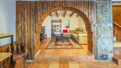 Rústica puerta arqueada de madera abre a sala con chimenea de piedra y vistas a las montañas en villa Masias Can Trabal