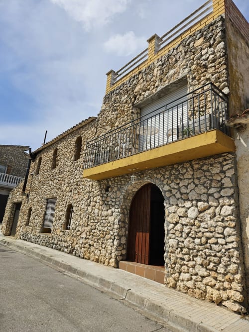 Villa histórica de piedra Masia Alt en Olèrdola con puerta de madera arqueada, balcón terraza amarillo y vistas a la montaña