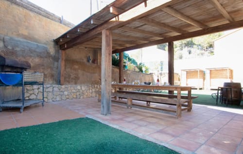 Terraza de comedor al aire libre en villa Masias Can Trabal con pérgola de madera, mesa de comedor y vistas a las montañas en Olèrdola
