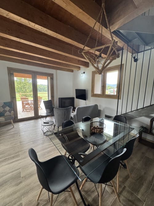 Sala de estar moderna en Cal Boix, Berga, con vigas de madera vista, mesa de comedor, sillas grises y vistas a la montaña