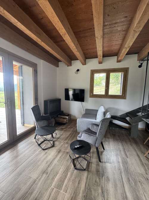 Sala moderna de la casa rural Cal Boix en Berga con vigas de madera vista, muebles grises, TV de pantalla plana y vistas a las montañas
