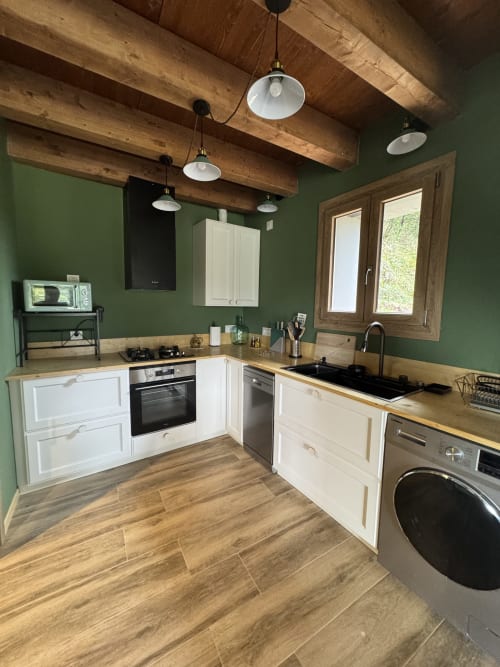 Cocina moderna de la casa rural Cal Boix en Berga, con muebles blancos, vigas de madera, paredes verdes y electrodomésticos de acero inoxidable