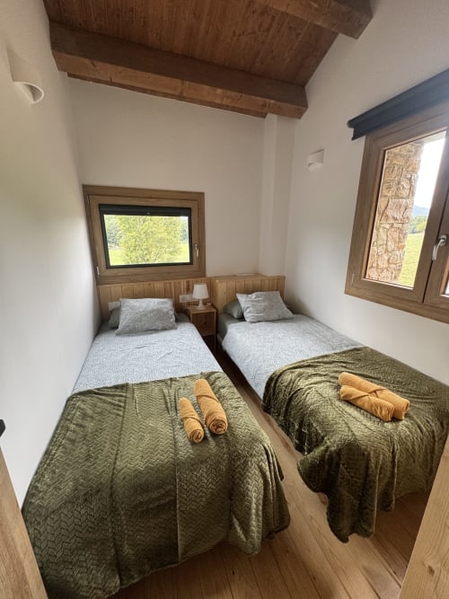 Dormitorio doble con colchas verdes en la casa rural Cal Boix de Berga, vistas montañosas desde ventanas de marco de madera