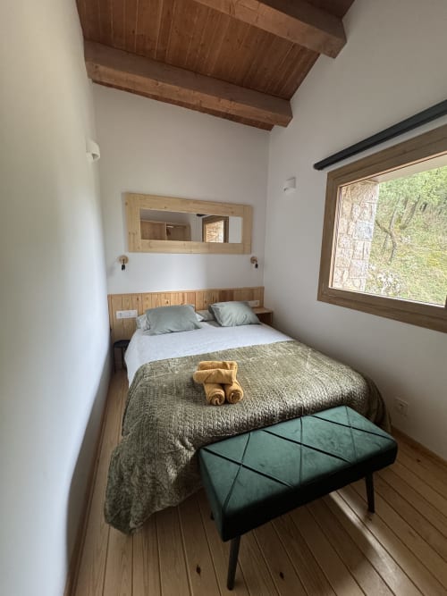Acogedor dormitorio en la casa rural Cal Boix de Berga con vigas de madera, cama de matrimonio, banco verde y vistas a la montaña