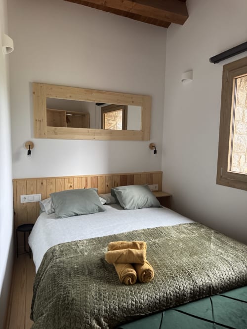 Dormitorio acogedor en la casa rural Cal Boix de Berga con cama de madera, ropa de cama gris, espejo y vistas a la montaña