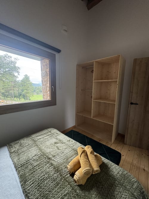 Dormitorio de la casita Cal Boix en Berga con muebles de madera, vistas a la montaña por la ventana y toallas enrolladas en la cama