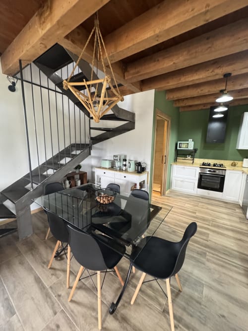 Comedor y cocina de concepto abierto en la casa rural Cal Boix, Berga, con escalera de caracol negra y vigas de madera