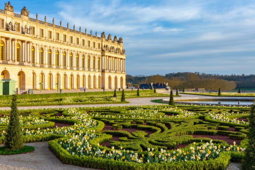 Façade grandiose du palais aux ornements raffinés surplombant des jardins formels avec fleurs blanches et haies à Colombes, France
