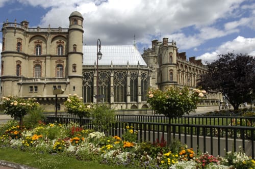 Château orné aux tours crème entouré de jardins fleuris et d'une clôture noire à Colombes, France