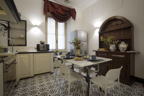 Elegante zona cucina-sala da pranzo nella Magna Mater Suite, Roma, con mobili color panna, tavolo in marmo e nicchia in legno scuro
