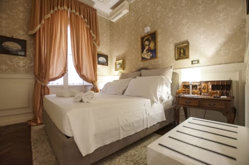 Elegante camera da letto presso Magna Mater Suite a Roma con biancheria bianca, arte decorativa incorniciata, tende in terracotta e stile classico