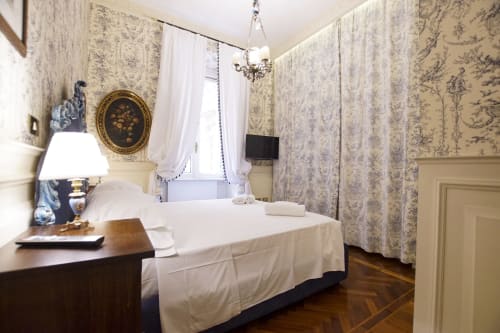 Camera della Magna Mater Suite a Roma con carta da parati toile, letto bianco, lampadario elegante e arredi d'epoca